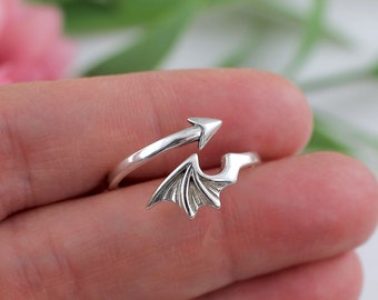 May include: A silver ring with a wing design. The ring is open and adjustable.