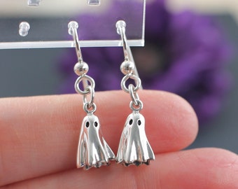 May include: A pair of silver dangle earrings featuring a ghost design. The ghosts have two small circles for eyes.