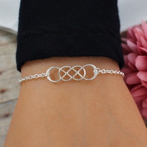 May include: A silver infinity symbol bracelet with a delicate chain. The bracelet is on a person's wrist.