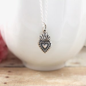 May include: A silver necklace with a detailed heart pendant. The heart has a smaller heart in the center and is surrounded by a decorative border.