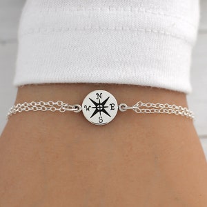 May include: A silver chain bracelet with a compass charm. The compass charm has a black and white design with the letters N, W, E, and S.
