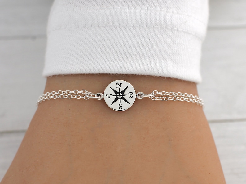 May include: A silver chain bracelet with a compass charm. The compass charm has a black and white design with the letters N, W, E, and S.