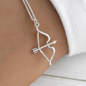 May include: A silver necklace with a bow and arrow pendant. The pendant is a simple design with a curved bow and a straight arrow.