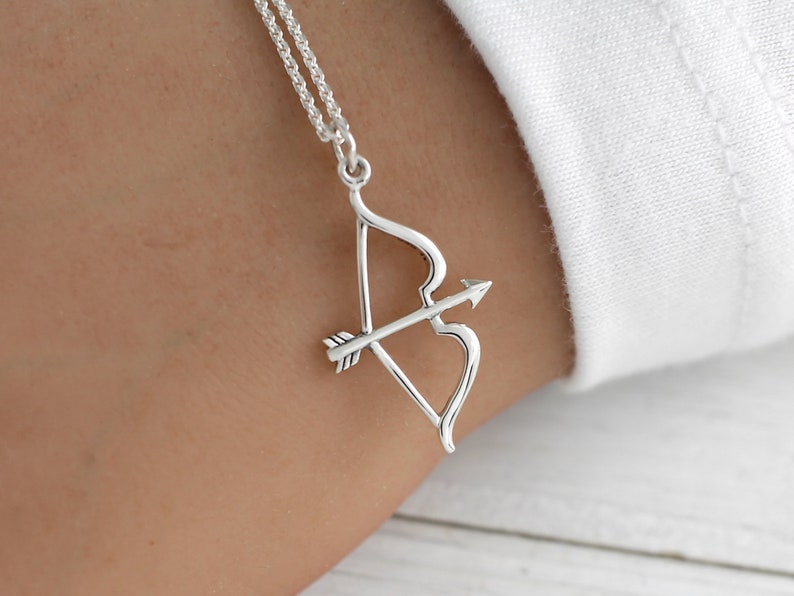 May include: A silver necklace with a bow and arrow pendant. The pendant is a simple design with a curved bow and a straight arrow.