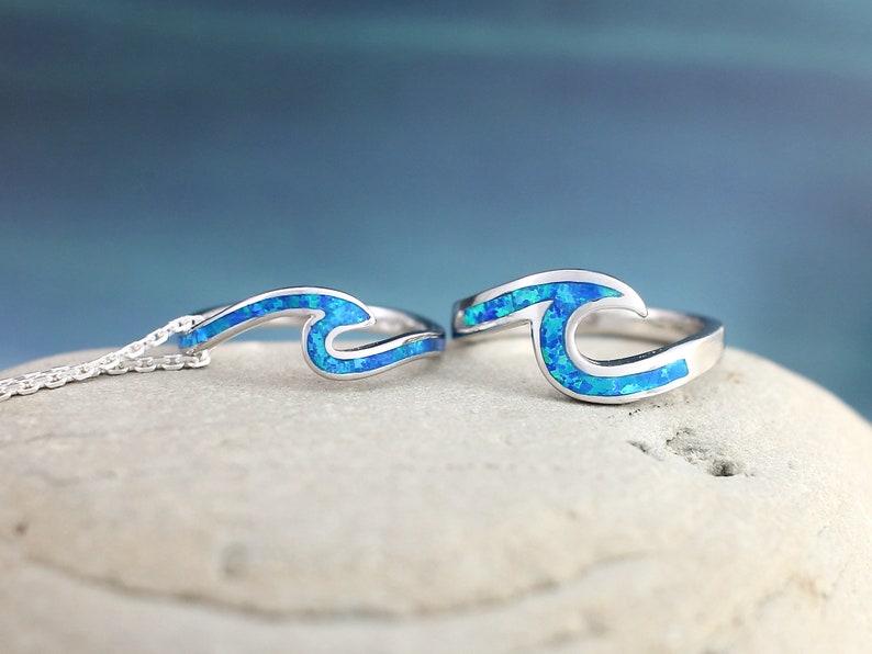 Puede incluir: Un conjunto de anillo y collar de plata con incrustaciones de &oacute;palo azul en forma de ola. El dise&ntilde;o de la ola es un s&iacute;mbolo popular del oc&eacute;ano y la playa.