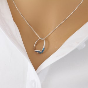 Puede incluir: Un collar de cadena de plata con un colgante de anillo de &oacute;palo azul.