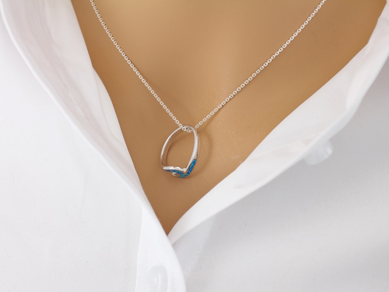 Puede incluir: Un collar de cadena de plata con un colgante de anillo de &oacute;palo azul.