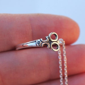 May include: A silver necklace with a key-shaped pendant. The key has three loops and a small detail on the handle.