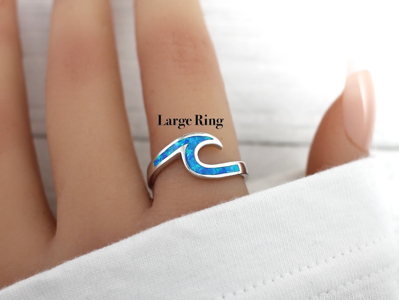 Puede incluir: Un anillo de plata con un dise&ntilde;o de ola de &oacute;palo azul. El anillo est&aacute; en un dedo y el texto "Large Ring" est&aacute; por encima del anillo.
