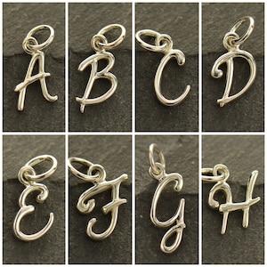 May include: Eight silver charm pendants in the shape of cursive letters A through H. Each charm has a loop at the top for attaching to a necklace or bracelet.