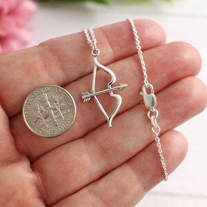 May include: A silver necklace with a bow and arrow pendant. The pendant is about the size of a dime.