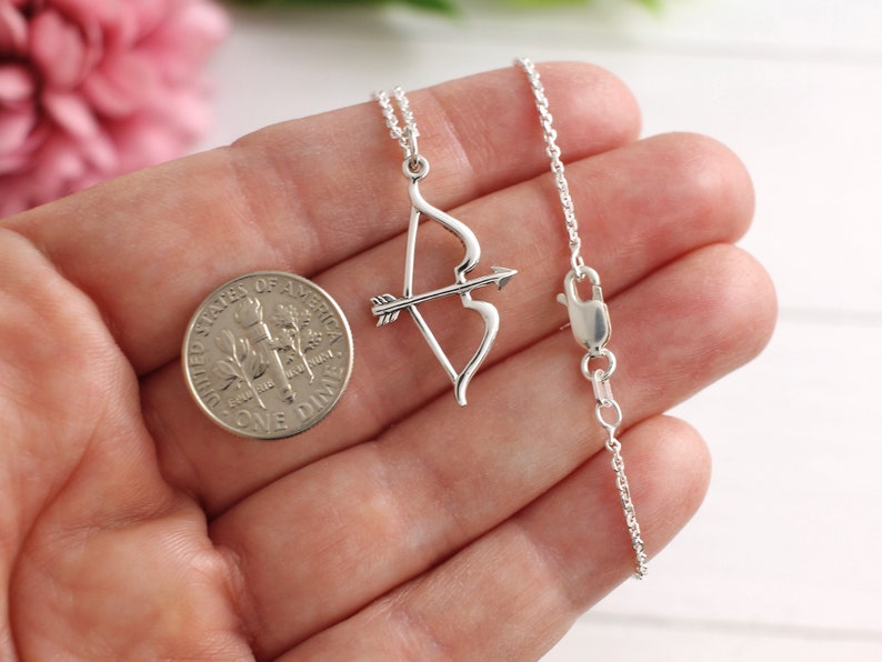 May include: A silver necklace with a bow and arrow pendant. The pendant is about the size of a dime.