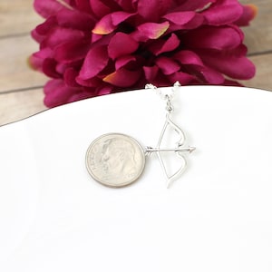 May include: A silver necklace with a bow and arrow pendant. The pendant is about the size of a dime.