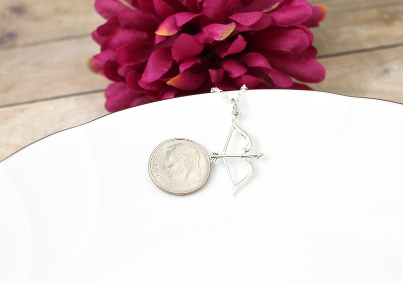 May include: A silver necklace with a bow and arrow pendant. The pendant is about the size of a dime.