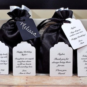 May include: Five small gift bags with tags. The tags have handwritten messages for different occasions, including a wedding, birthday, and a thank you. The bags are black satin with silver ribbon ties.