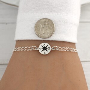 May include: A silver chain bracelet with a compass charm. The compass charm is round and has the letters N, W, E, and S printed on it.