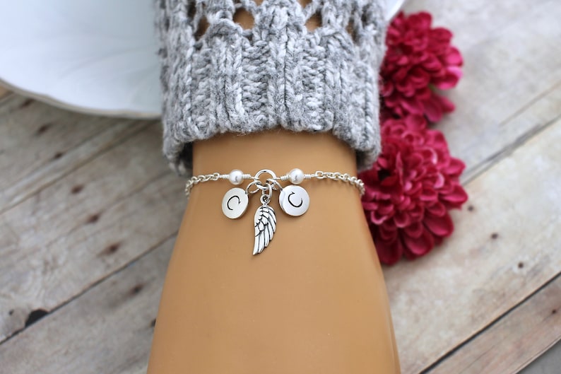 May include: A silver chain bracelet with two silver charms that say "C" and a silver angel wing charm.