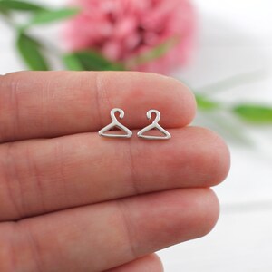 May include: A pair of silver hanger-shaped stud earrings. The earrings are small and delicate, and they are perfect for adding a touch of whimsy to any outfit.