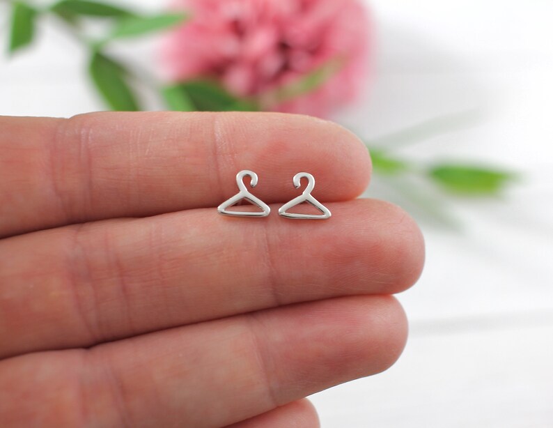 May include: A pair of silver hanger-shaped stud earrings. The earrings are small and delicate, and they are perfect for adding a touch of whimsy to any outfit.