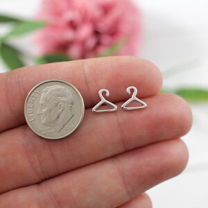 May include: Two silver hanger shaped earrings on a hand with a US dime for scale.