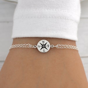 May include: A silver chain bracelet with a compass charm. The compass charm has a black and white design with the letters N, S, E, and W.
