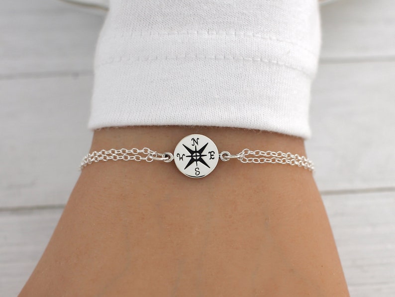 May include: A silver chain bracelet with a compass charm. The compass charm has a black and white design with the letters N, S, E, and W.