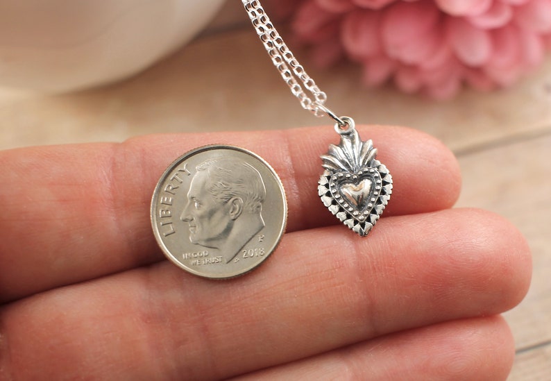 May include: A silver necklace with a small, detailed silver heart pendant. The heart has a gold center and is surrounded by a decorative border. The pendant is about the size of a dime.