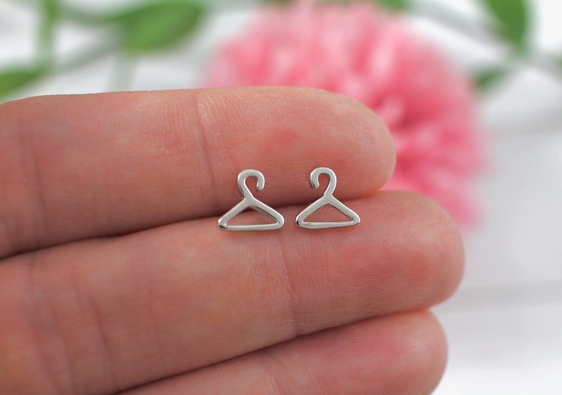 May include: A pair of silver hanger-shaped stud earrings. The earrings are small and delicate, and they are perfect for adding a touch of whimsy to any outfit.