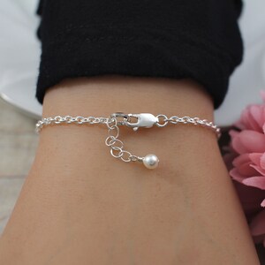 May include: A silver chain bracelet with a small pearl charm. The bracelet is on a person's wrist.
