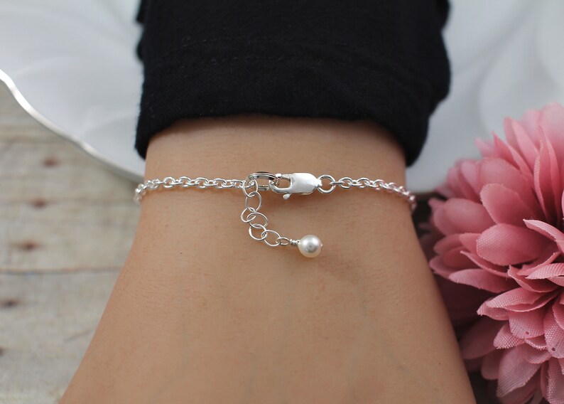 May include: A silver chain bracelet with a small pearl charm. The bracelet is on a person's wrist.