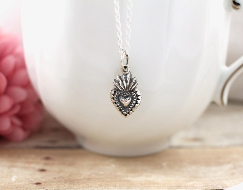 May include: A silver necklace with a detailed heart pendant. The heart has a smaller heart in the center and is surrounded by a decorative border.