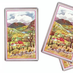 May include: Three rectangular playing cards with a landscape painting. The artwork depicts a valley with red-roofed buildings, trees, and mountains under a cloudy sky. The cards have a white border with a pink inner line.