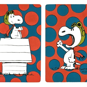 May include: Two Snoopy illustrations on playing cards. One shows Snoopy sitting on his doghouse, wearing a pilot's cap and red scarf. The other shows Snoopy with his mouth open and arm raised. The background is red with blue circles.