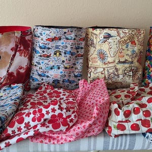 May include: A collection of fabric tote bags and matching fabric items. The bags feature various patterns, including a 49ers logo, race cars, travel maps, and dice. Coordinating fabric items include floral and cherry patterns.