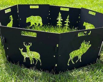 Könnte beinhalten: Schwarzer Metall-Feuerstellenschirm mit ausgeschnittenen Silhouetten von Wildtieren, darunter ein Bär, ein Hirsch und Bäume. Der achteckige Schirm hat Griffe und steht auf grünem Gras.