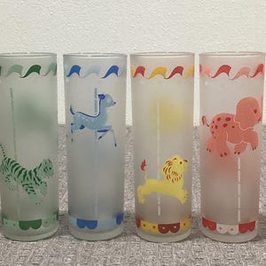 May include: Set of eight frosted glass tumblers with carousel animal designs. Each glass features a different animal, including a zebra, giraffe, tiger, dog, lion, turtle, and horse. The glasses have colorful accents and a scalloped base.