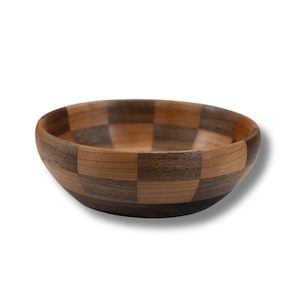 May include: A wooden bowl with a checkerboard pattern. The bowl is made of alternating squares of light and dark wood, creating a visually appealing design. The bowl is round and has a smooth finish.