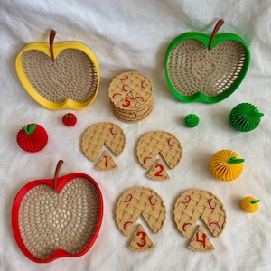May include: A set of educational toys including three apple-shaped trays in yellow, green, and red, several tan circular pie-shaped pieces with red numbers one through five, and small spherical paper honeycomb apples in red, green, and yellow.