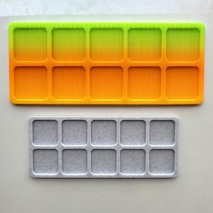 May include: Two rectangular trays with ten square compartments each. The top tray has a gradient of green to orange. The bottom tray is gray. Both trays have a ribbed texture.