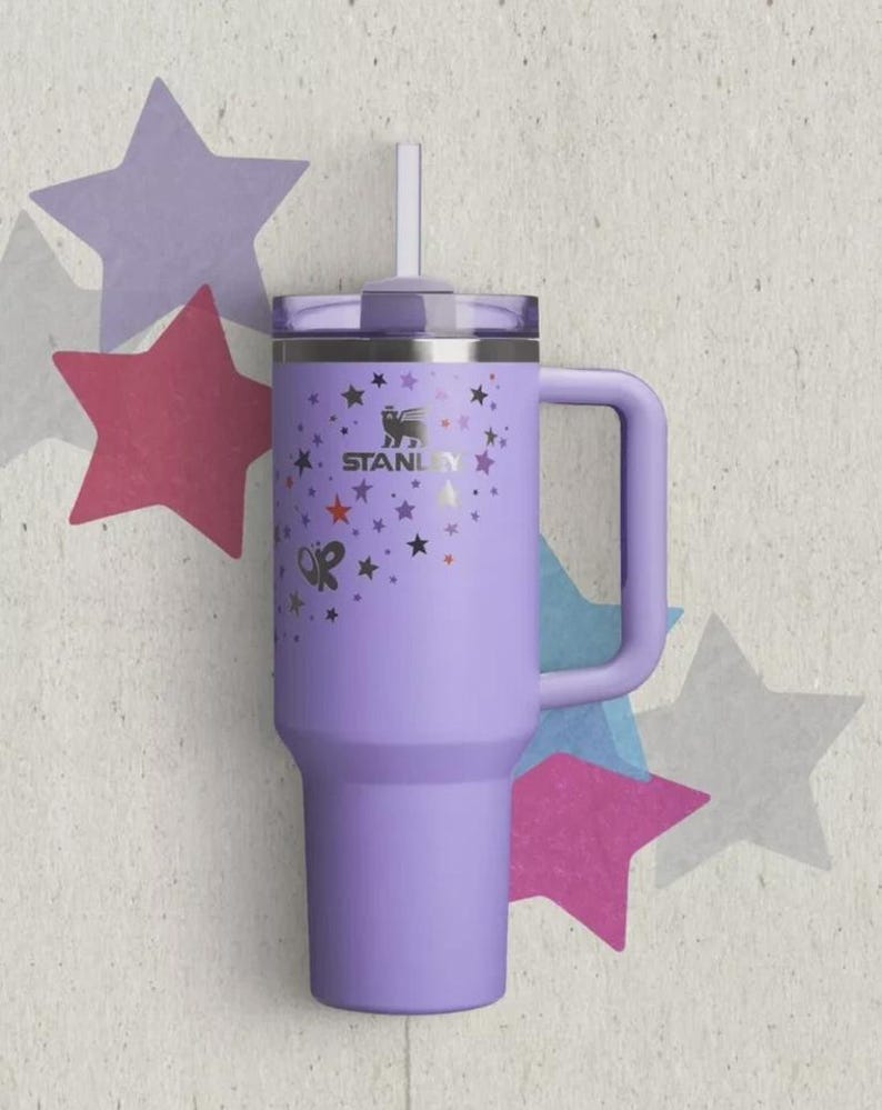 May include: A light purple stainless steel tumbler with a handle, a clear lid, and a straw. The exterior features the Stanley logo and a pattern of small stars in black, red, and purple, along with the letters OP printed on the side of the cup.