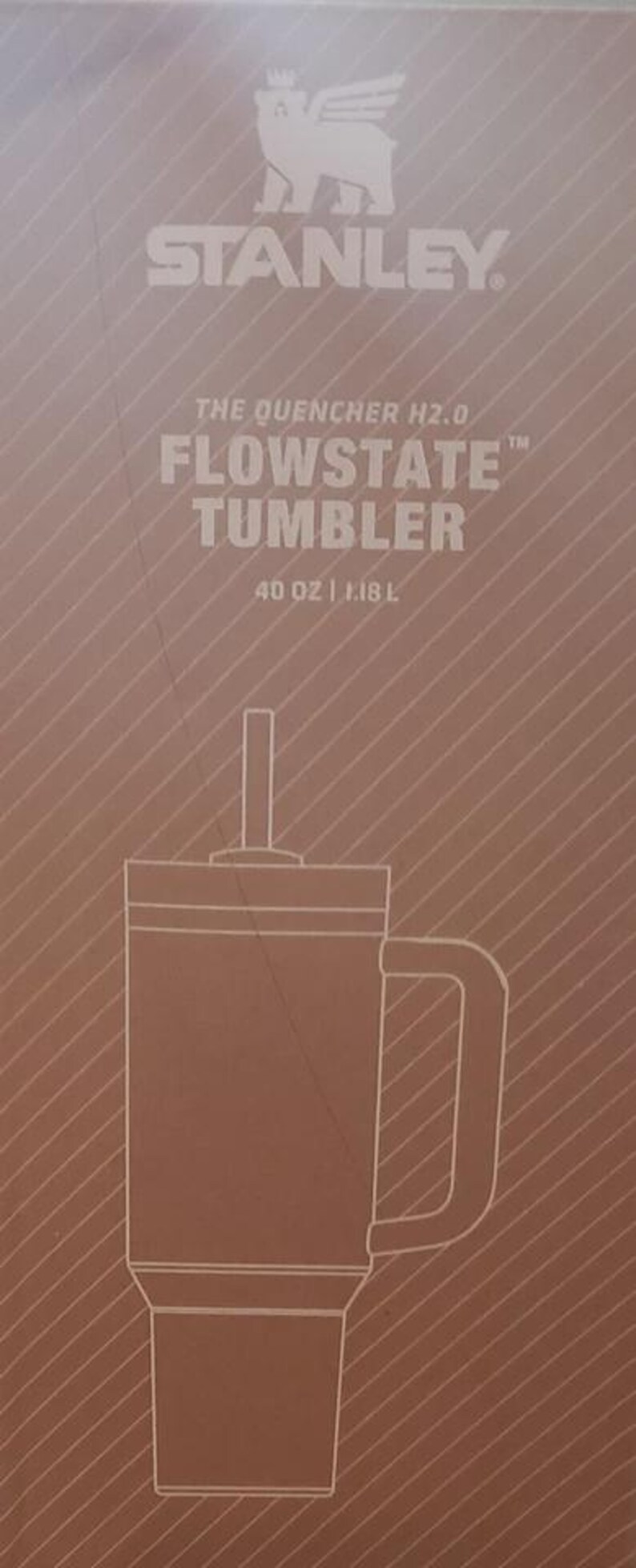 K&ouml;nnte beinhalten: Eine braune Produktverpackung f&uuml;r einen Stanley The Quencher H2.0 Flowstate Becher mit einem Fassungsverm&ouml;gen von 1,18 L. Die Box zeigt eine wei&szlig;e Strichzeichnung des Bechers mit Strohhalm und Henkel sowie das Markenlogo und den Produktnamen.