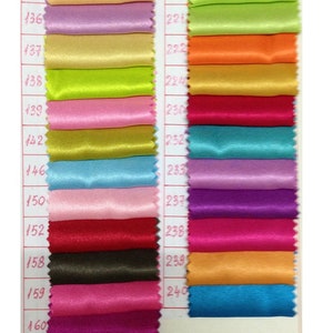 May include: A color swatch chart featuring various shades of satin fabric. The chart displays a range of colors, including black, beige, purple, green, pink, and blue. Each color is labeled with a number, providing a comprehensive color palette for design and craft projects.
