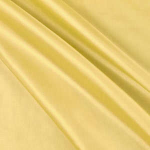 May include: A close-up shot of a folded, golden-yellow fabric. The fabric has a smooth, shiny texture, with visible folds and creases creating shadows and highlights. The color is a warm, light yellow, and the fabric appears to be lightweight.