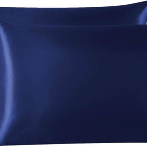 May include: Two navy blue satin pillowcases. The pillowcases are rectangular with a smooth, shiny texture. The colour is a deep, rich blue, and the fabric appears to be tightly woven. The pillowcases are designed for sleeping and home decor.