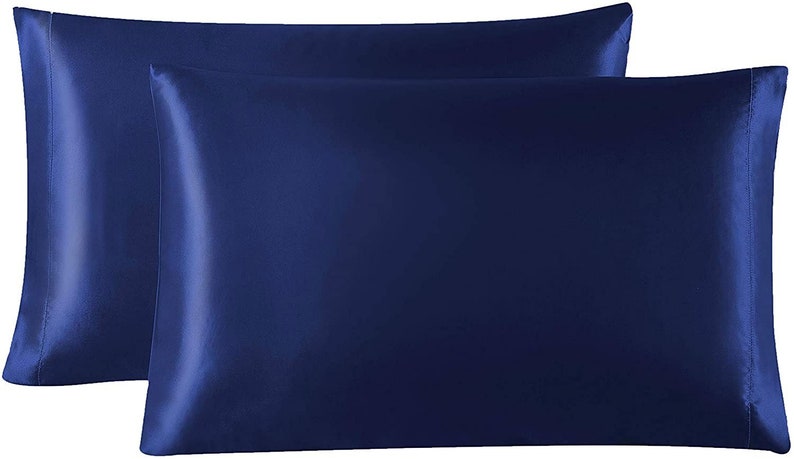 May include: Two navy blue satin pillowcases. The pillowcases are rectangular with a smooth, shiny texture. The colour is a deep, rich blue, and the fabric appears to be tightly woven. The pillowcases are designed for sleeping and home decor.