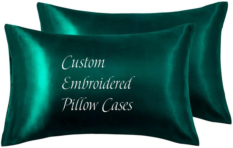 May include: Two emerald green satin pillowcases. The pillowcases have a lustrous sheen and the words "Custom Embroidered Pillow Cases" are written in white script across the front.