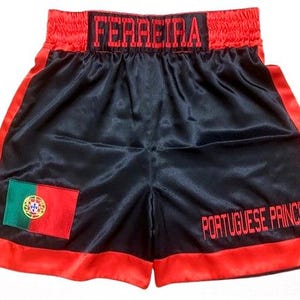 Op de afbeelding: Zwarte boksshorts met rode bies en tailleband. De shorts hebben de naam "FERREIRA" over de tailleband en de tekst "PORTUGUESE PRINCE" op de pijp. Een Portugese vlagpatch is op de voorkant genaaid.