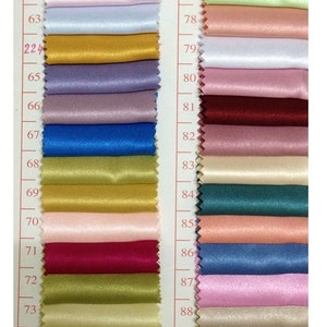 May include: A color swatch card featuring a variety of satin fabric samples. The samples are arranged in vertical rows, showcasing a spectrum of colors including white, pink, blue, gold, purple, and green. Each swatch is approximately 2 inches wide.