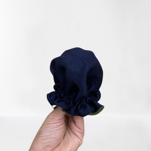 Könnte beinhalten: Eine marineblaue Haube mit gerüschtem Rand. Die Haube ist aus einem weichen Stoff gefertigt und hat ein kontrastierendes grünes Futter, das am Rand sichtbar ist. Der Artikel wird vor einem weißen Hintergrund gehalten.