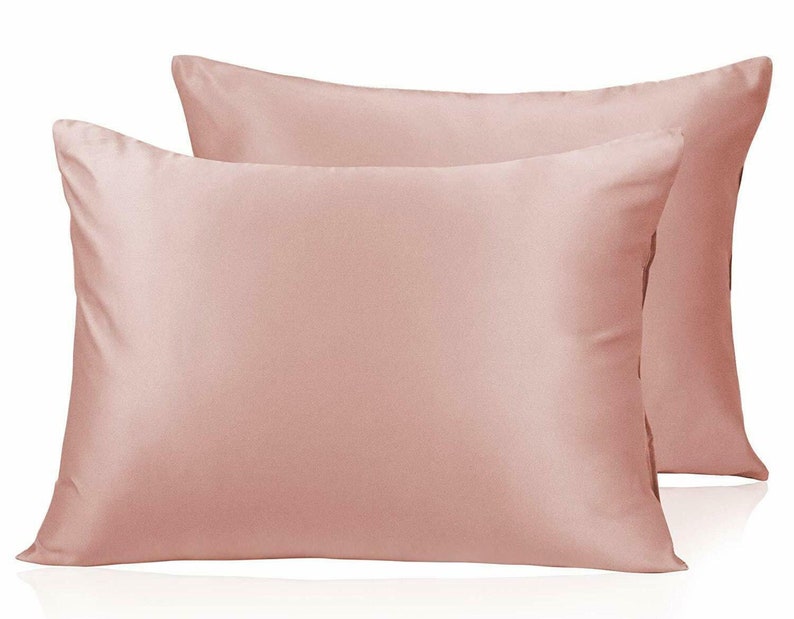 May include: Two blush-pink satin pillowcases. The rectangular pillows have a smooth, shiny finish. The pillowcases are displayed on a white background. The pillowcases are a solid colour and appear to be made of a soft material.